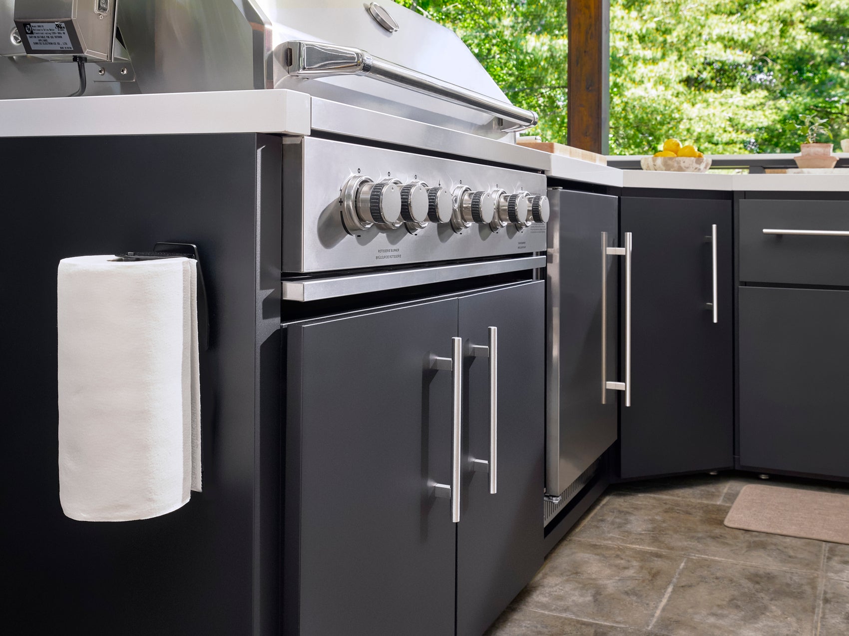 Emory Outdoor kitchen with dark gray cabinets, built-in grill, stainless steel countertop, paper towel holder.