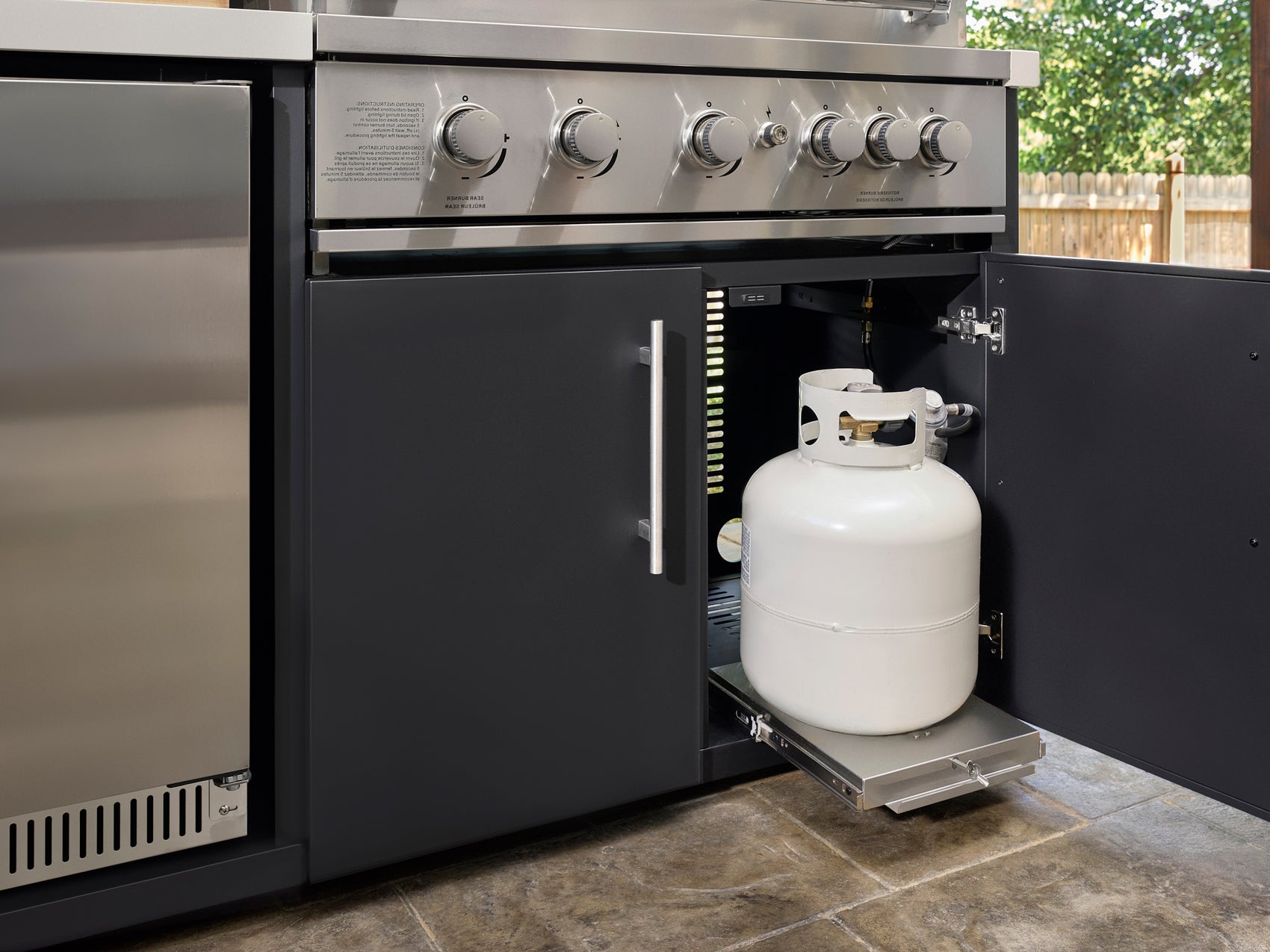 Emory outdoor kitchen with a stainless steel grill, propane tank on a slide-out drawer, and cabinetry under a steel roof.