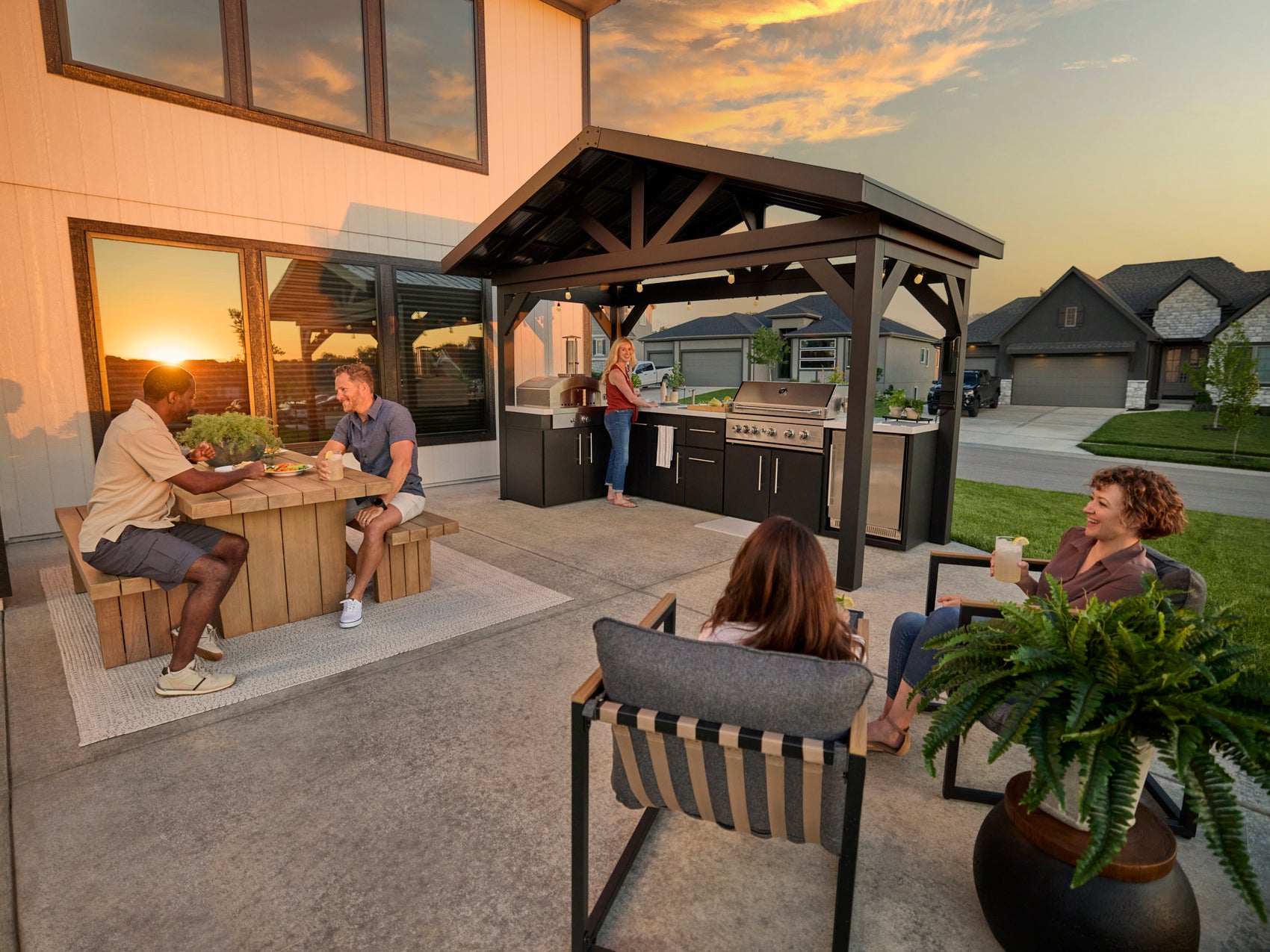 Covered patio kitchen with L-shaped marble countertops, gas grill and peak steel roof at sunset