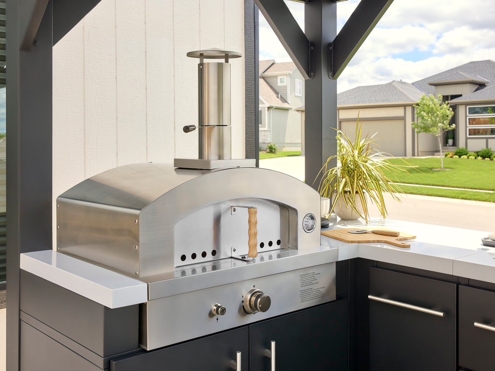 Stainless steel outdoor pizza oven closed on prefab outdoor kitchen with dark cabinetry