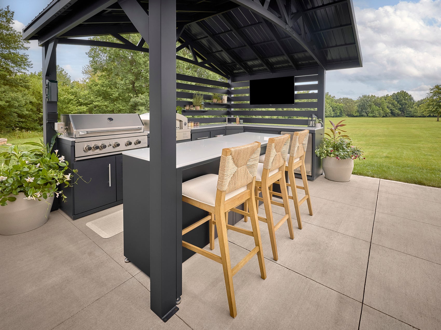 Langston Outdoor bar area with engineered stone countertop, built-in grill, four woven bar stools, and covered pavilion.