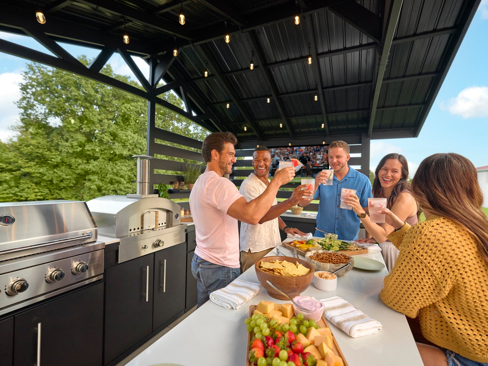 Group toasting with cocktails under the black powder-coated steel roof of the Langston outdoor kitchen.