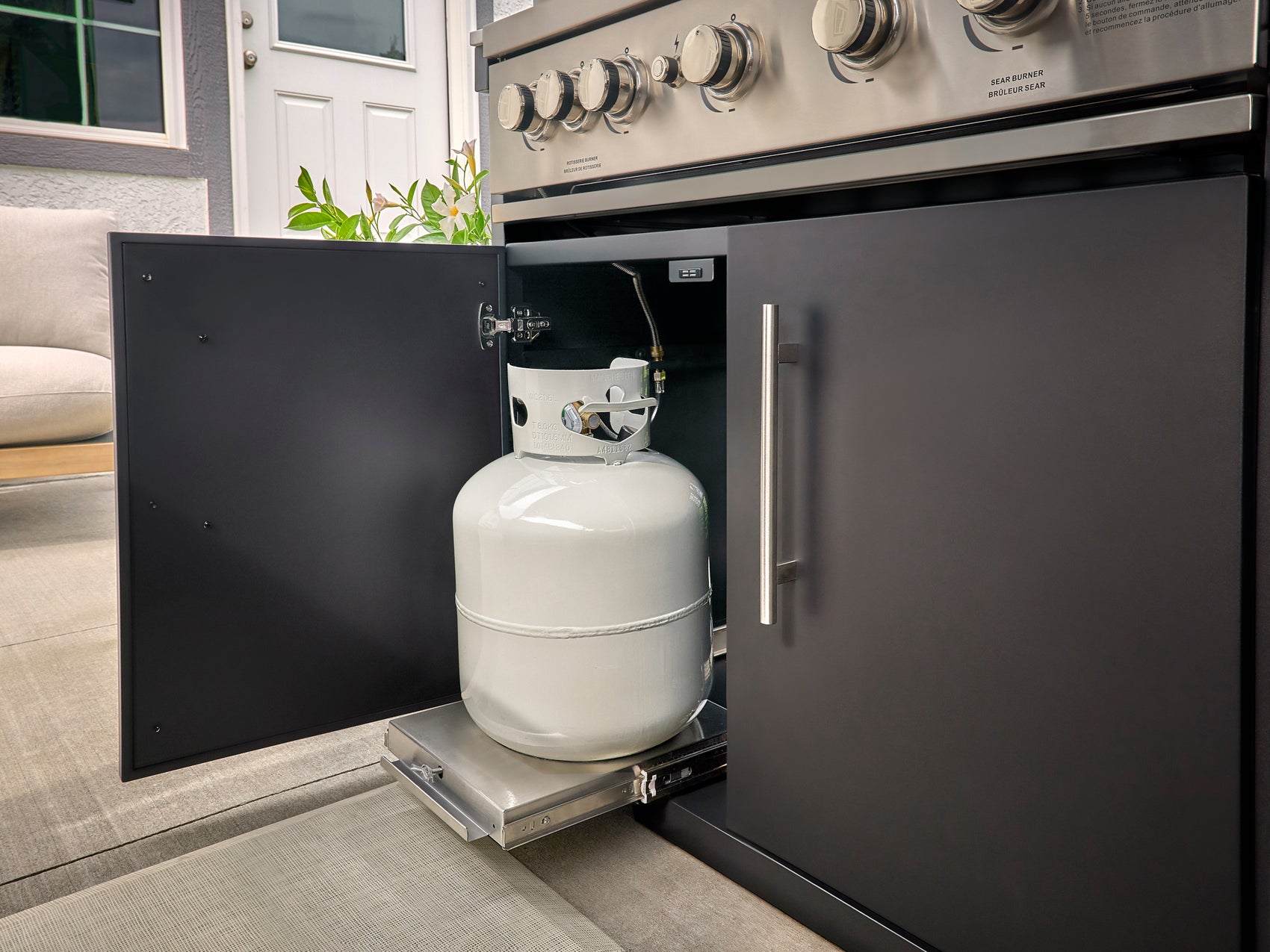 Propane tank stored on pull-out drawer in cabinet beneath stainless steel range in Langston modern kitchen.