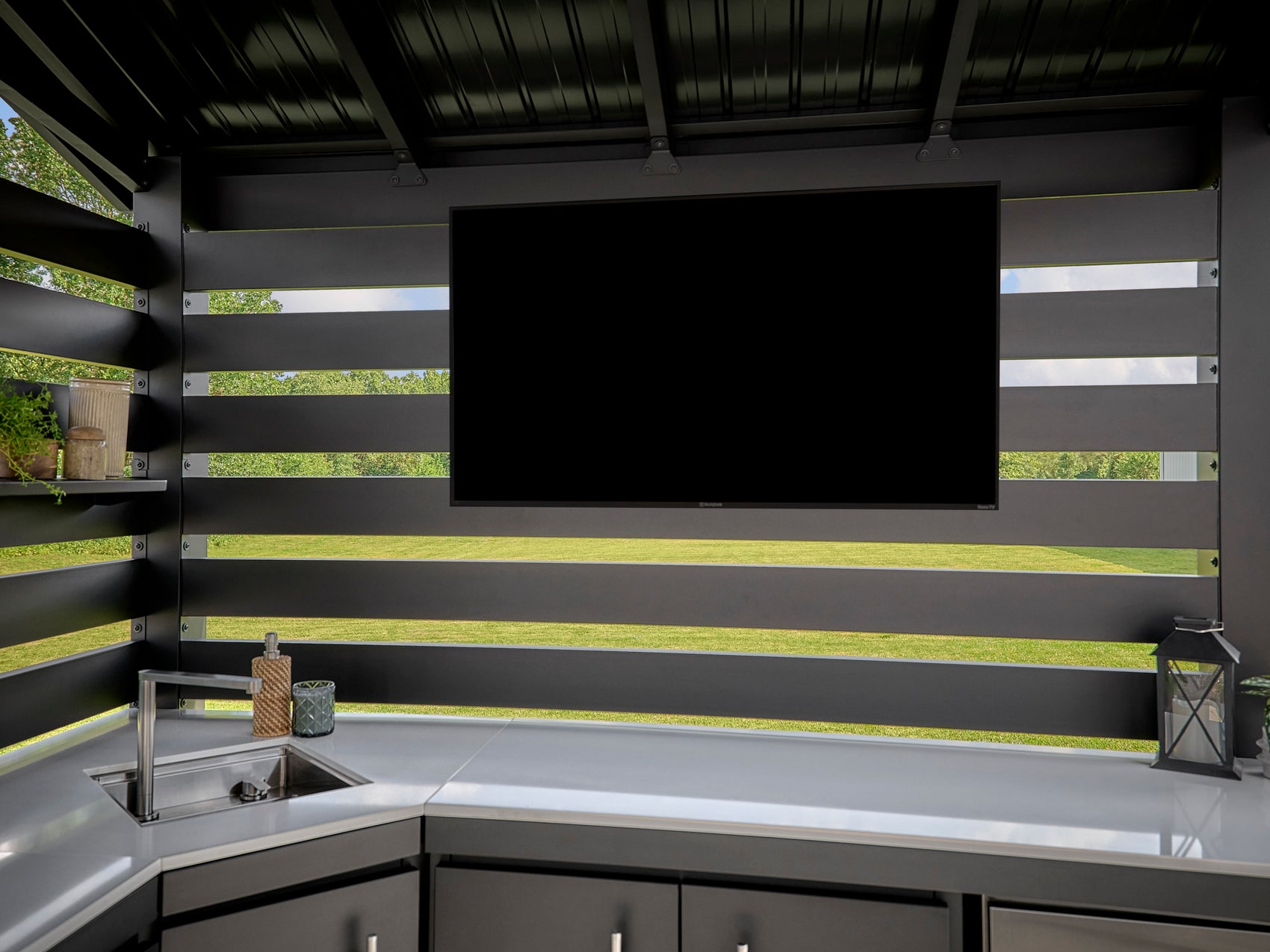 Range Outdoor Living Langston covered backyard kitchen with large wall-mounted TV, curved white countertop.