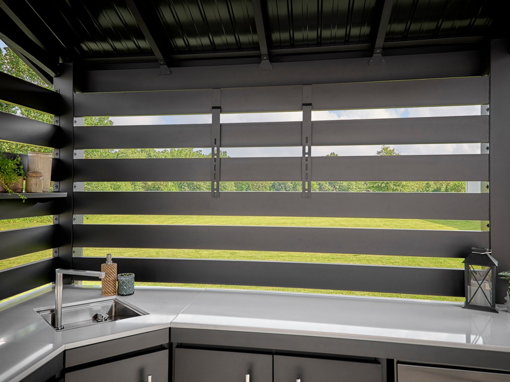 Langston modern outdoor kitchen under a dark gray steel roof with horizontal privacy slats and a white countertop.