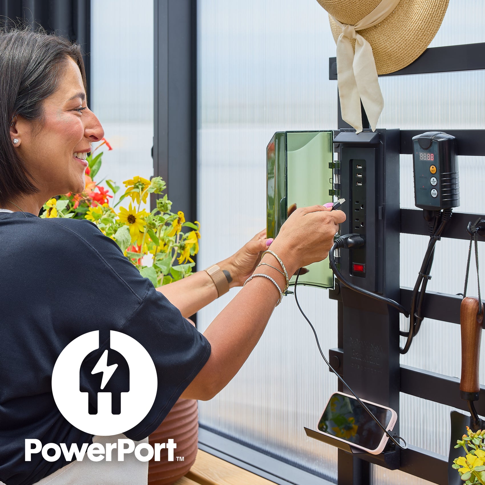 Woman using the PowerPort electric hub, which has three outlets and three USB ports, included with the Larkspur greenhouse.