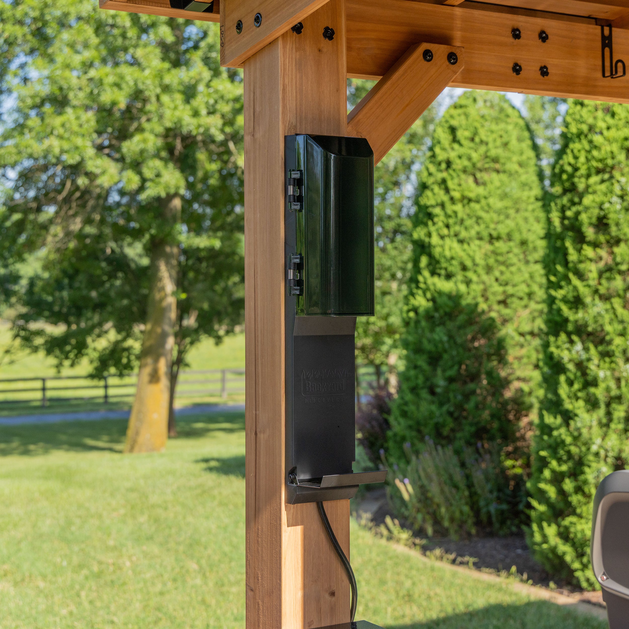 Weatherproof electrical outlet with cover on cedar post of backyard discovery grill gazebo in yard.