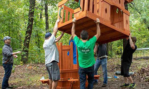 Workers constructing a wooden playset in a forest clearing.