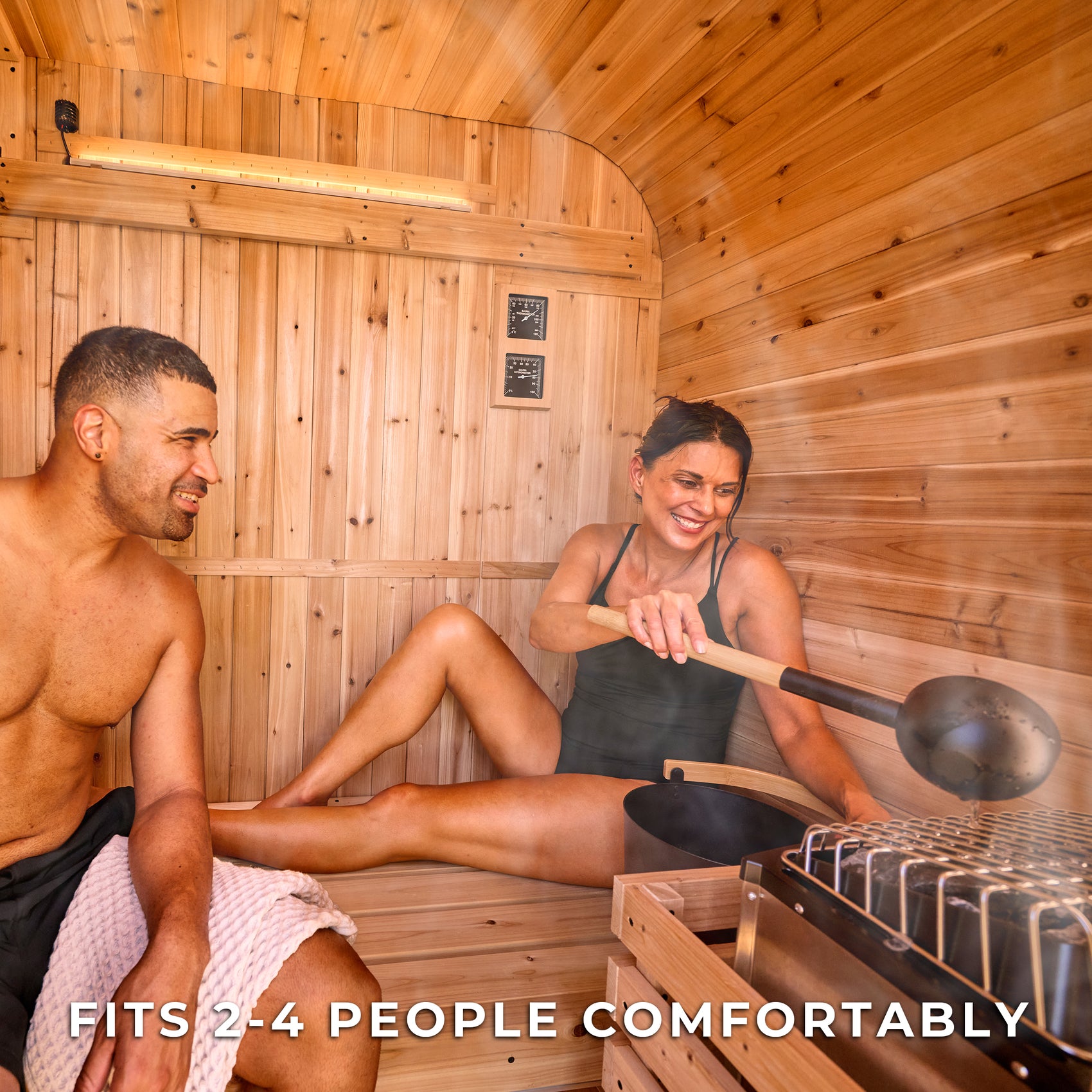 Couple enjoying Finnish steam inside Lennon 2-4 person traditional cube sauna pouring water on hot stones with ladle