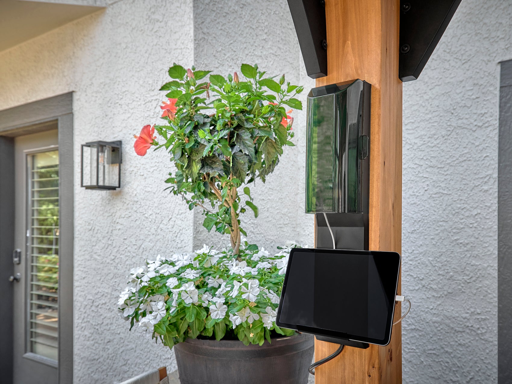 Tablet mounted on wood post of steel Lodge patio gazebo with power outlet and flowering plants in planter.