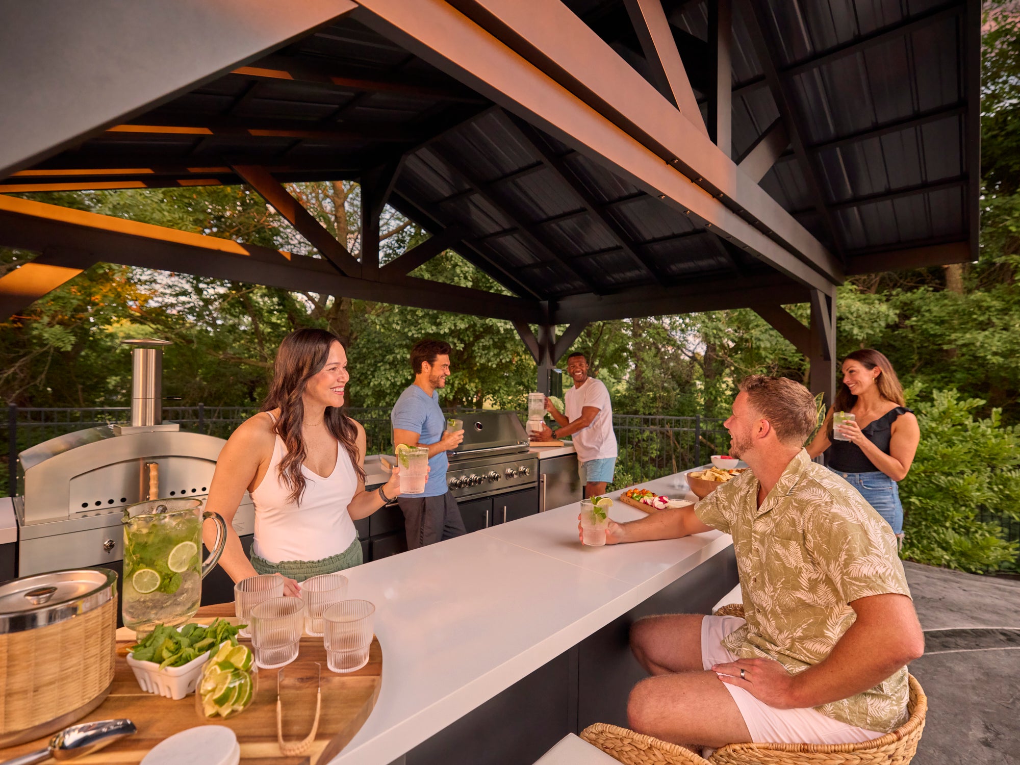 Range Outdoor Living Lancaster galley kitchen with guests dining and grilling in landscaped backyard setting.