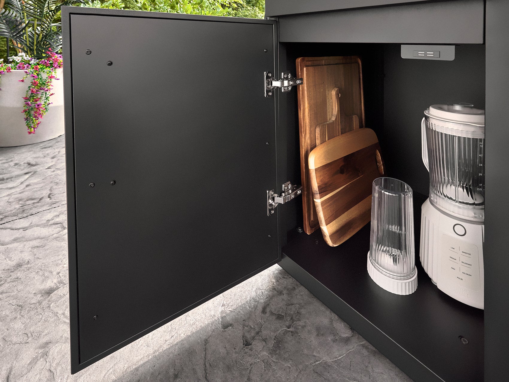 Open matte black outdoor storage cabinet revealing wooden cutting boards and blender on countertop in Emory modern kitchen.