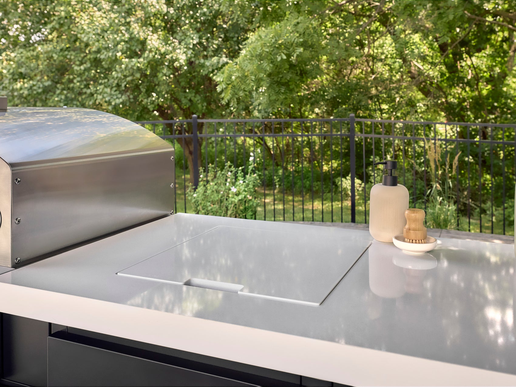 Recessed bar sink with flush cover in engineered stone kitchen countertop next to stainless steel grill on outdoor deck.