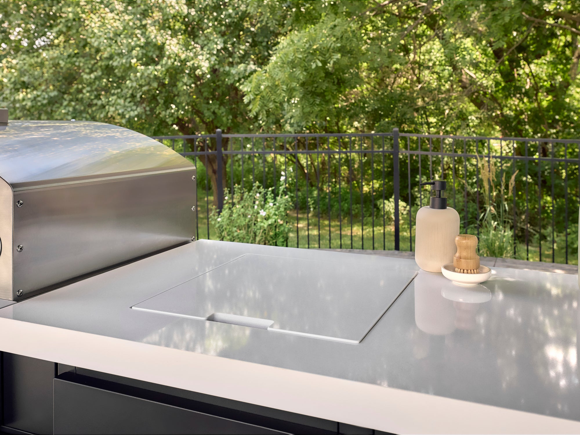 Recessed bar sink with flush cover in engineered stone kitchen countertop next to stainless steel grill on outdoor deck.