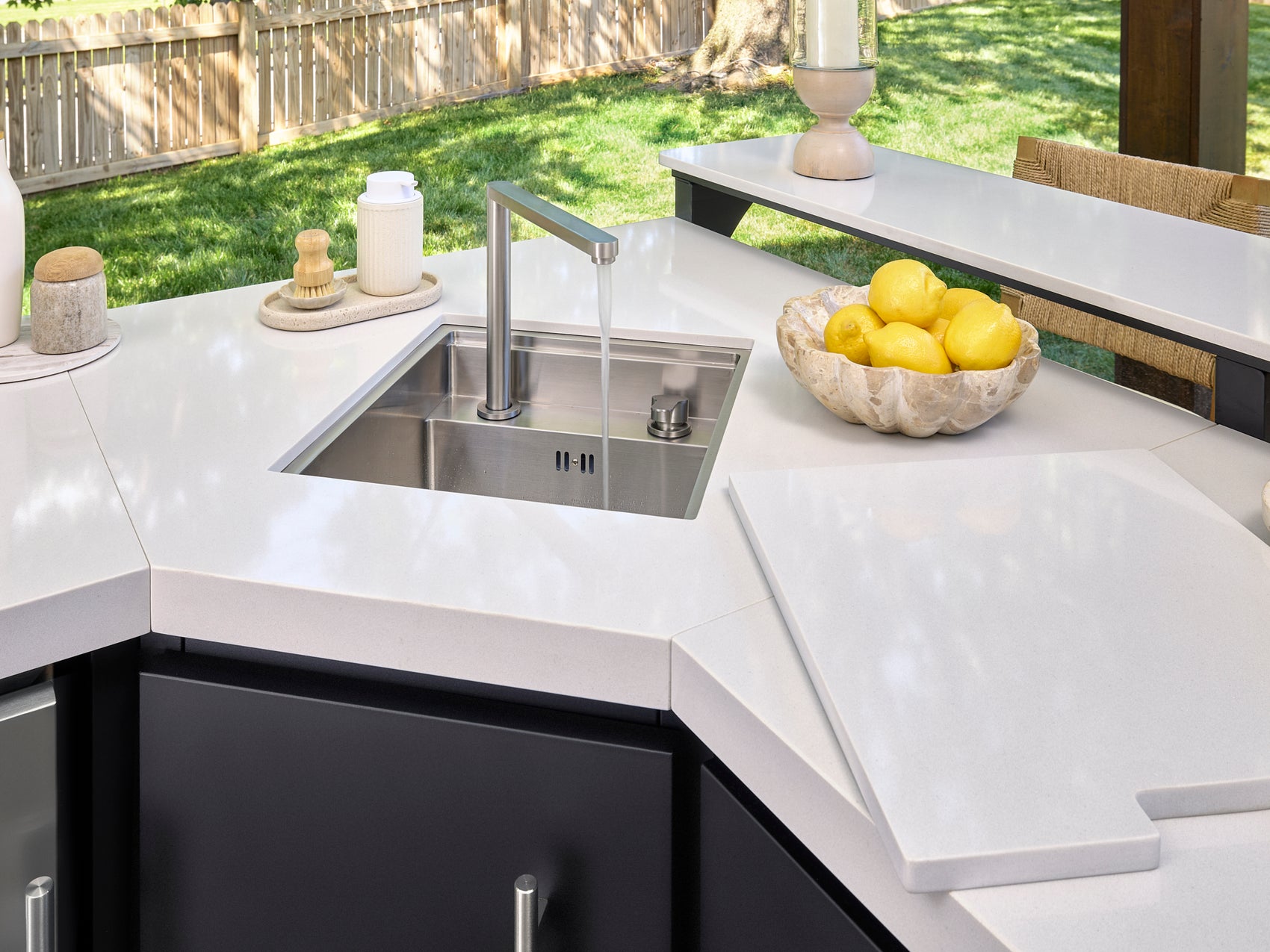 Undermount stainless steel sink with modern faucet set in white engineered stone Emory outdoor kitchen countertop.