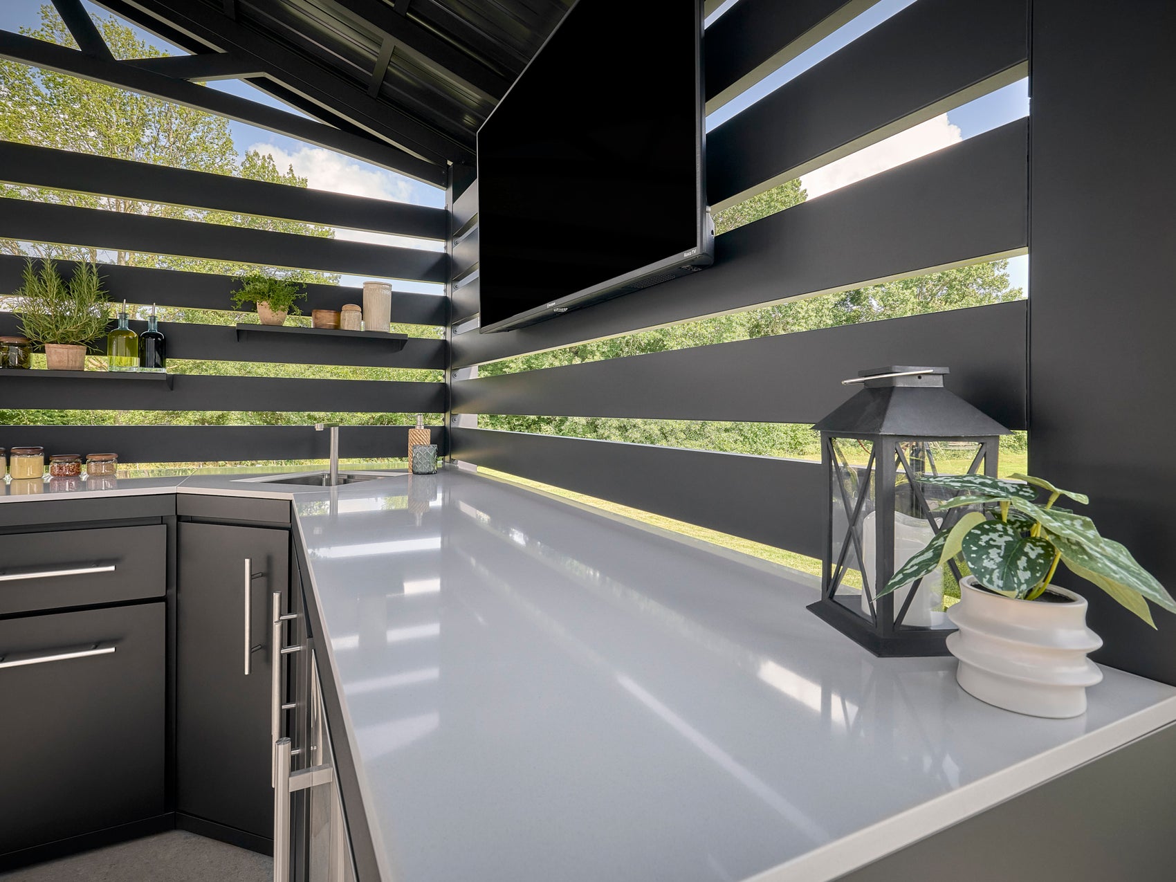 White engineered stone countertop on Langston outdoor kitchen with shade overhead and potted plant beside lantern.