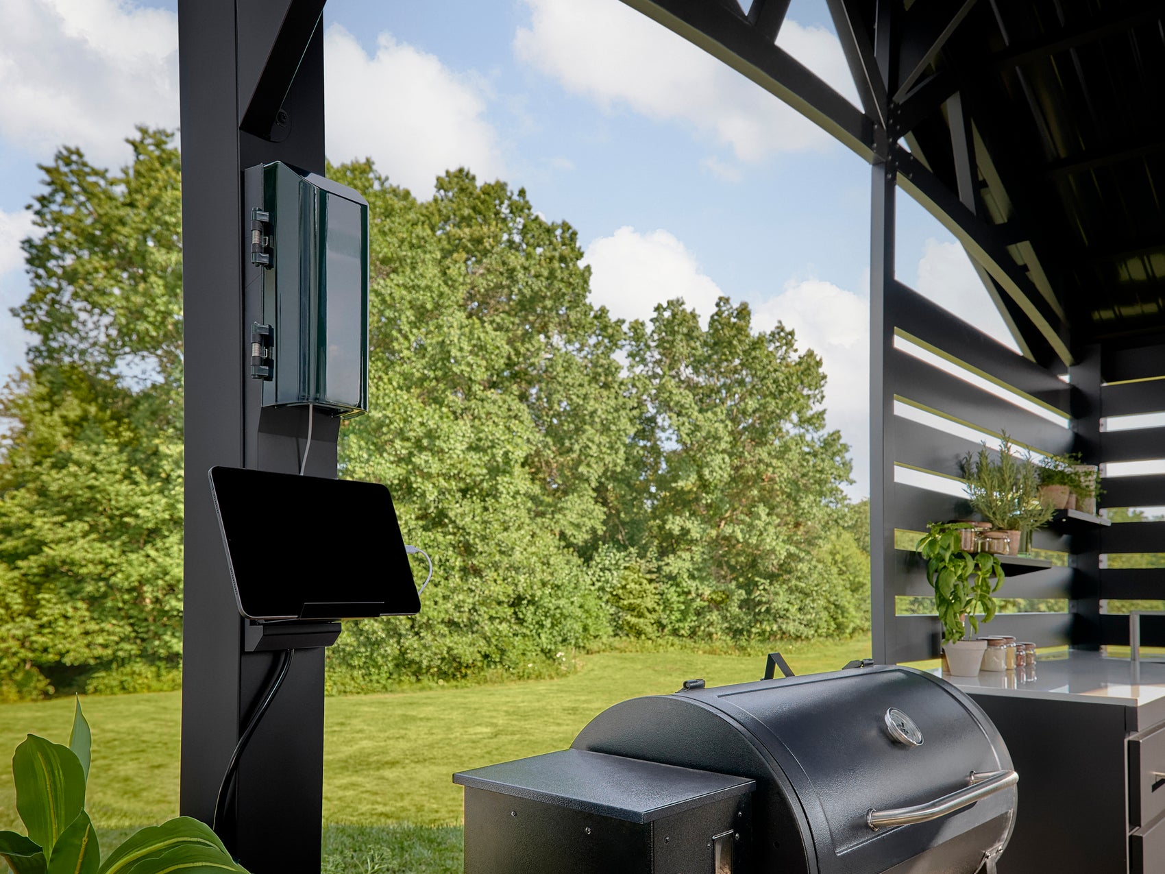 Outdoor electrical outlet and tablet mount installed on black steel kitchen post beside built-in grill station.