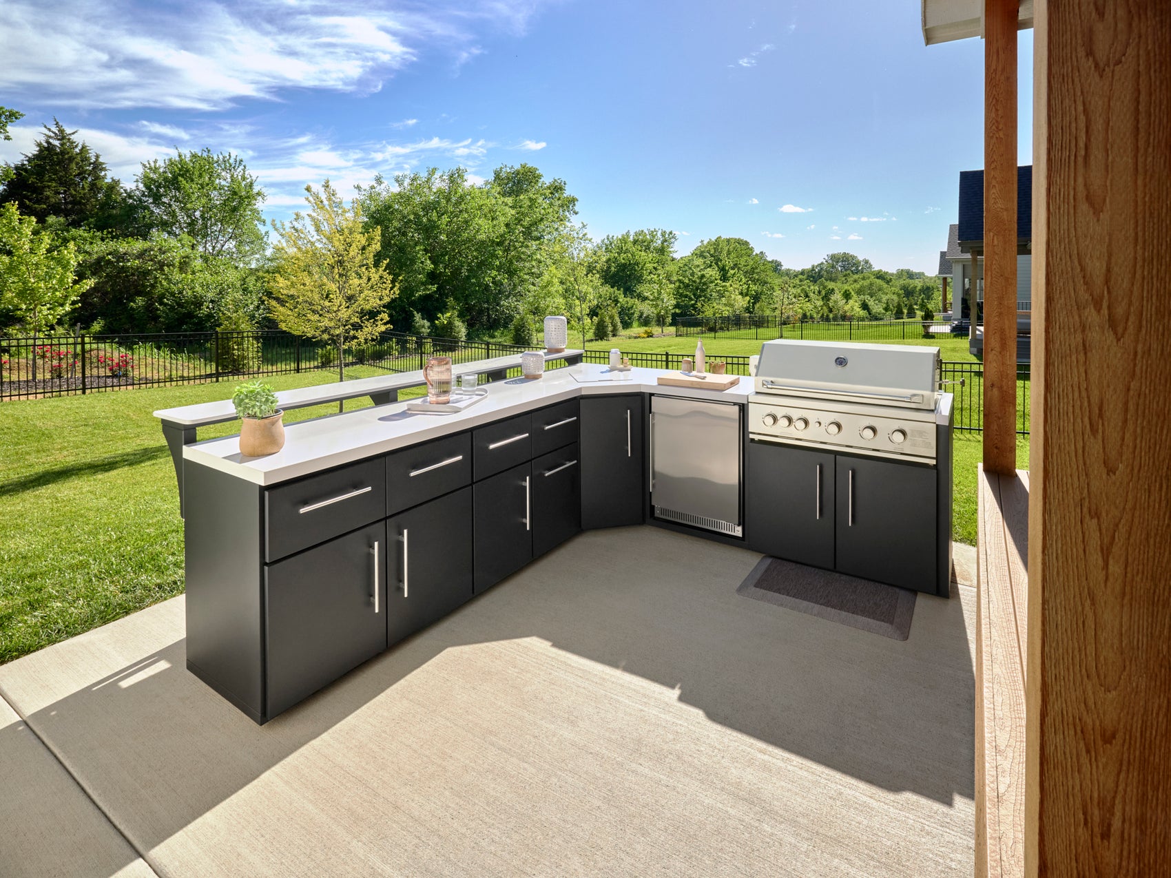 L-shaped Emory backyard kitchen with dark cabinets, engineered stone countertop, built-in grill, and refrigerator on patio.