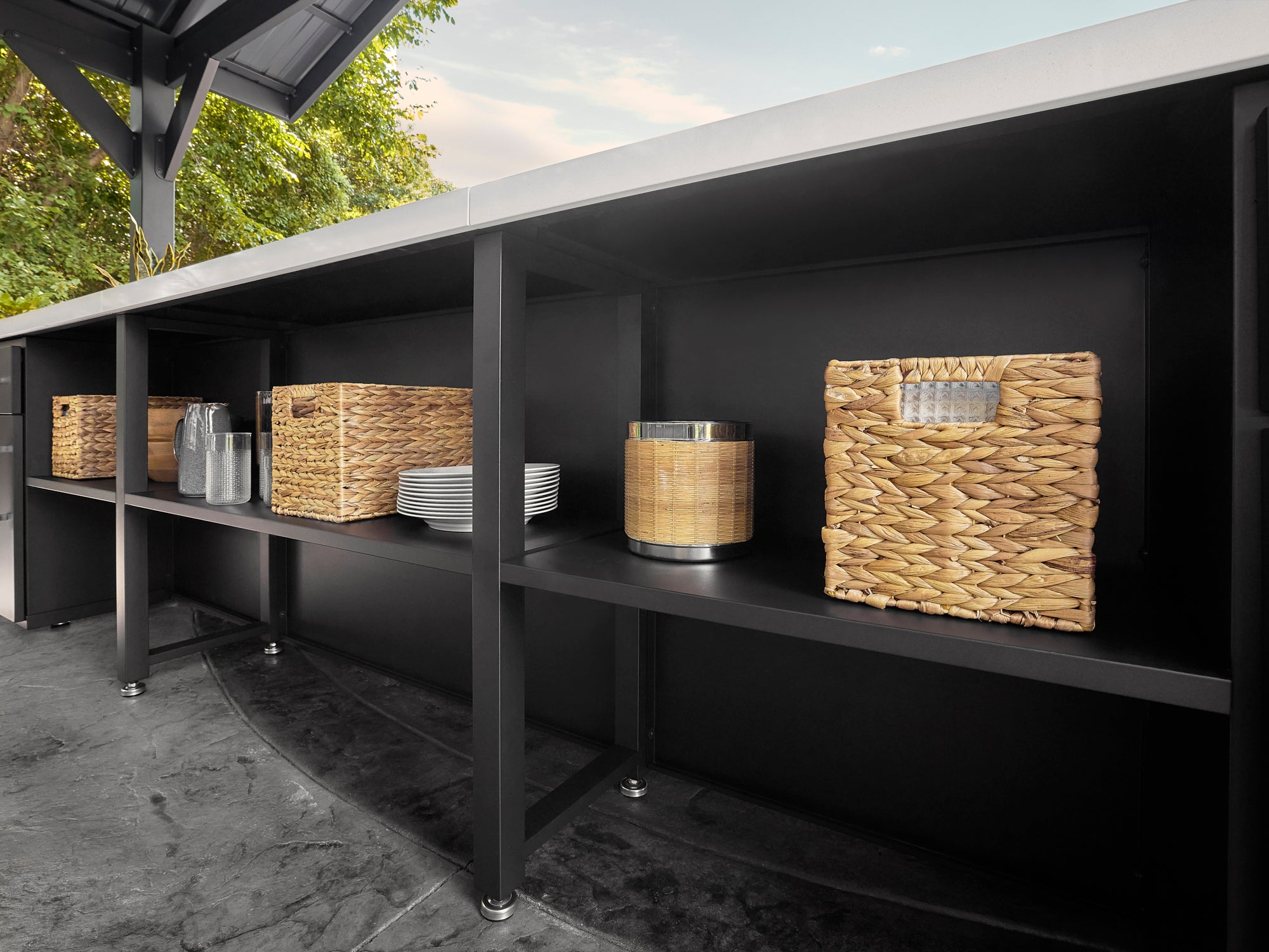 Lancaster galley kitchen powder-coated steel shelving unit with woven storage baskets and white plates in outdoor setting.