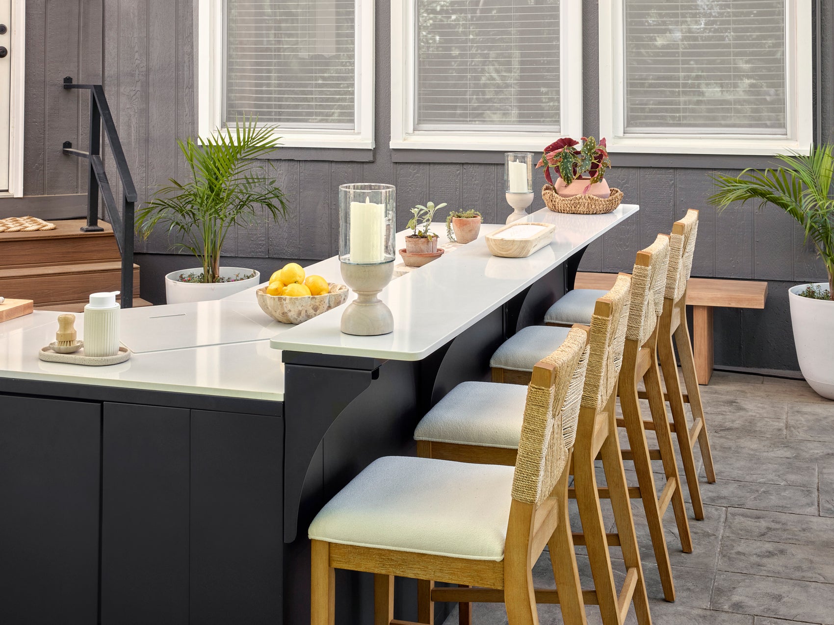 Emory modern outdoor bar with curved black cabinetry, white engineered stone countertop, four woven counter stools.