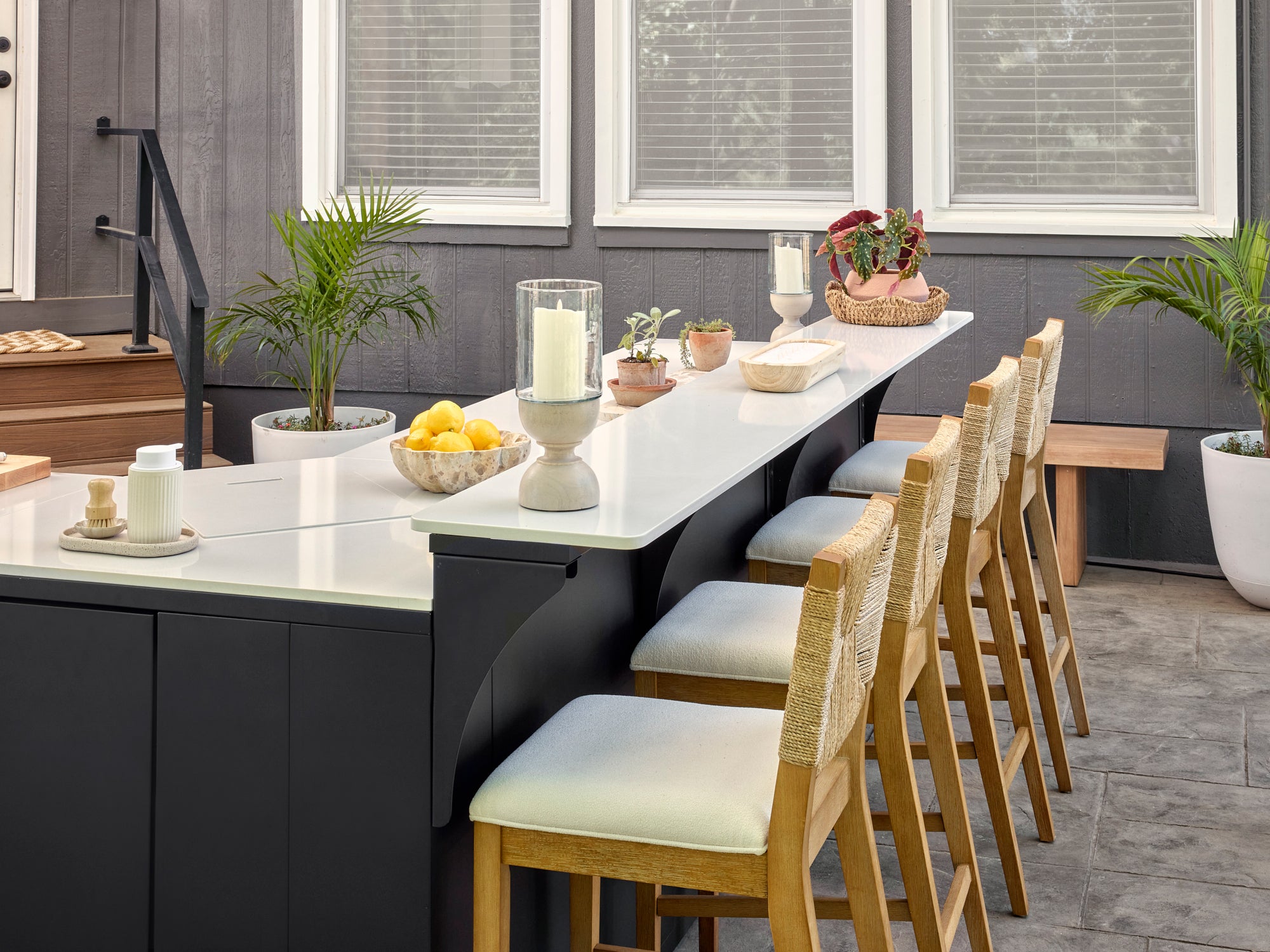 Emory modern outdoor bar with curved black cabinetry, white engineered stone countertop, four woven counter stools.