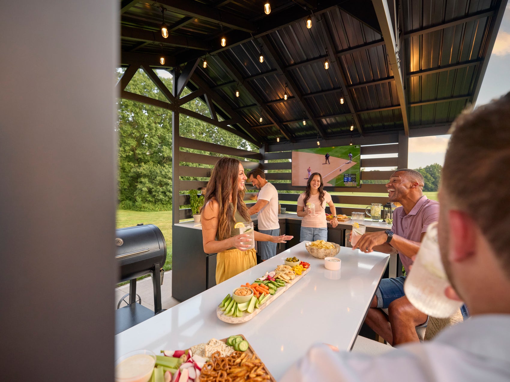 Langston modern outdoor kitchen covered pavilion with engineered stone counters, grill, and guests socializing outdoors.