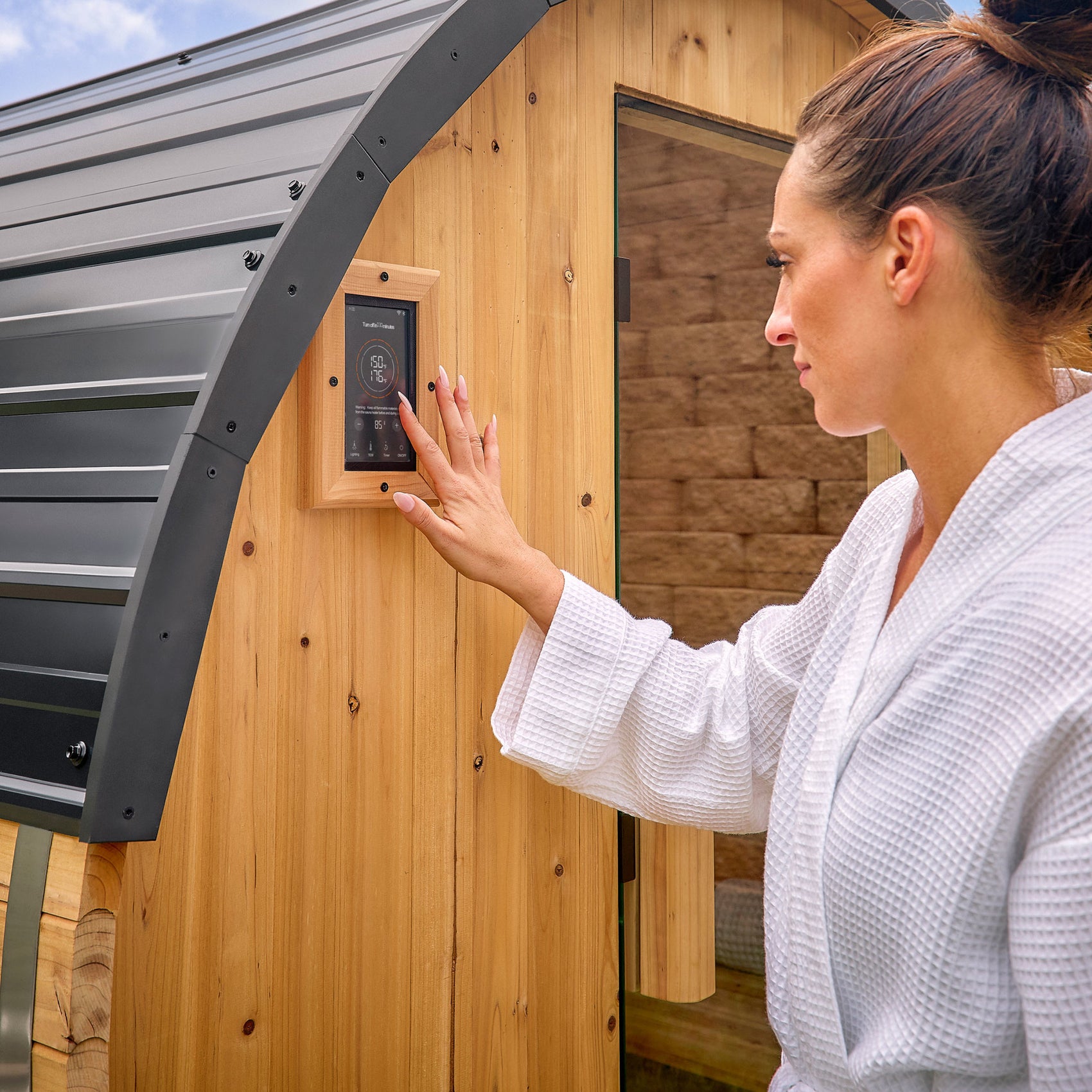 Woman adjusting digital temperature control panel on Paxton outdoor cedar barrel home sauna