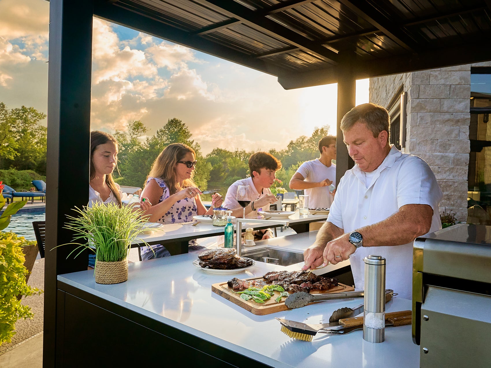 Man cutting meat on engineered stone counter in Edgemont Bay outdoor kitchen, designed with bar seating.