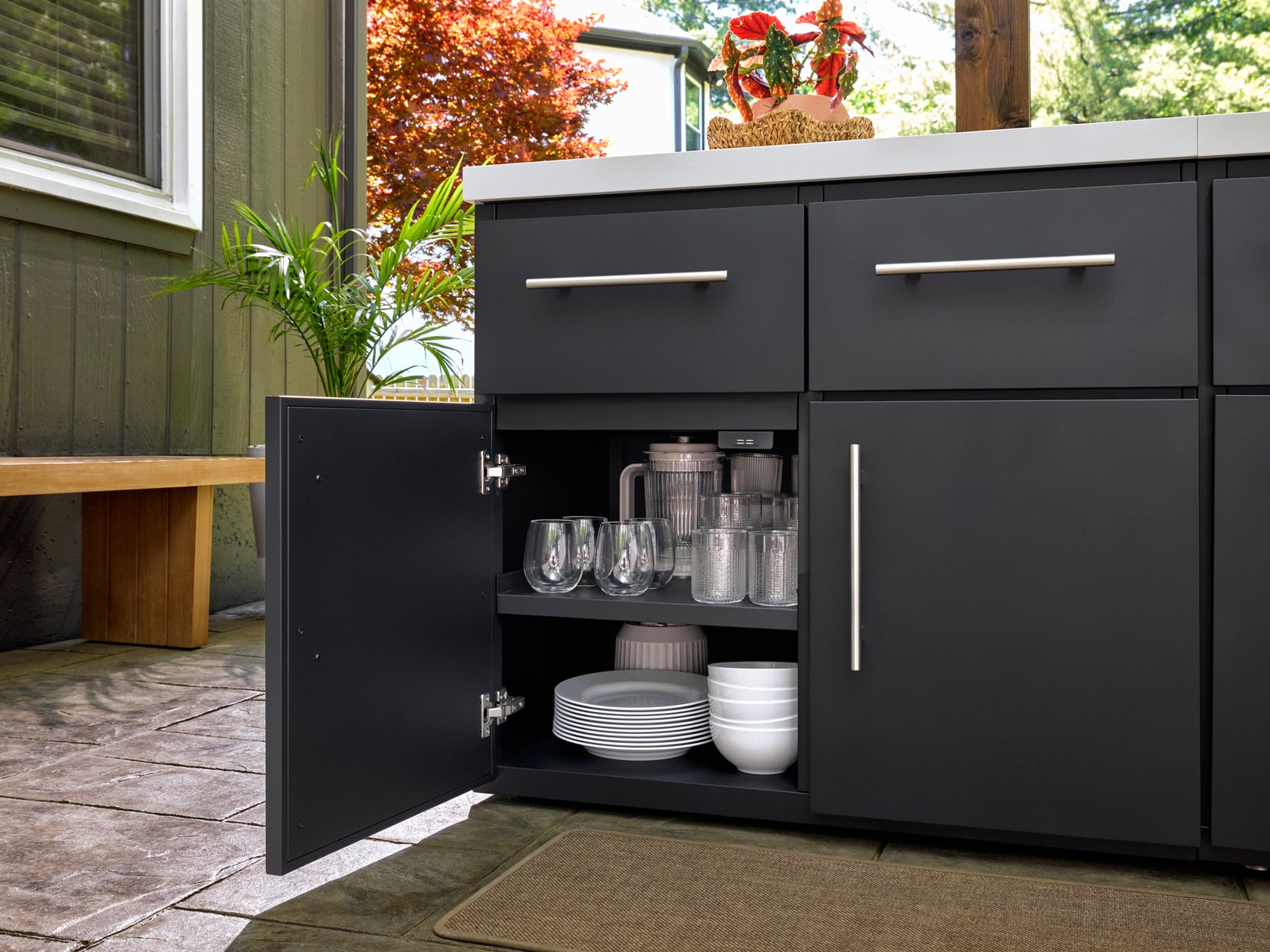 Emory outdoor kitchen cabinet with organized glassware, plates, and bowls on interior shelves, with brushed metal handle.