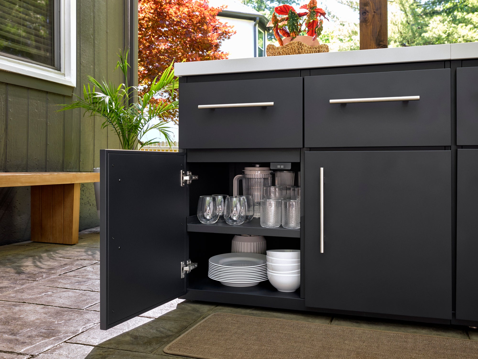 Emory outdoor kitchen cabinet with organized glassware, plates, and bowls on interior shelves, with brushed metal handle.