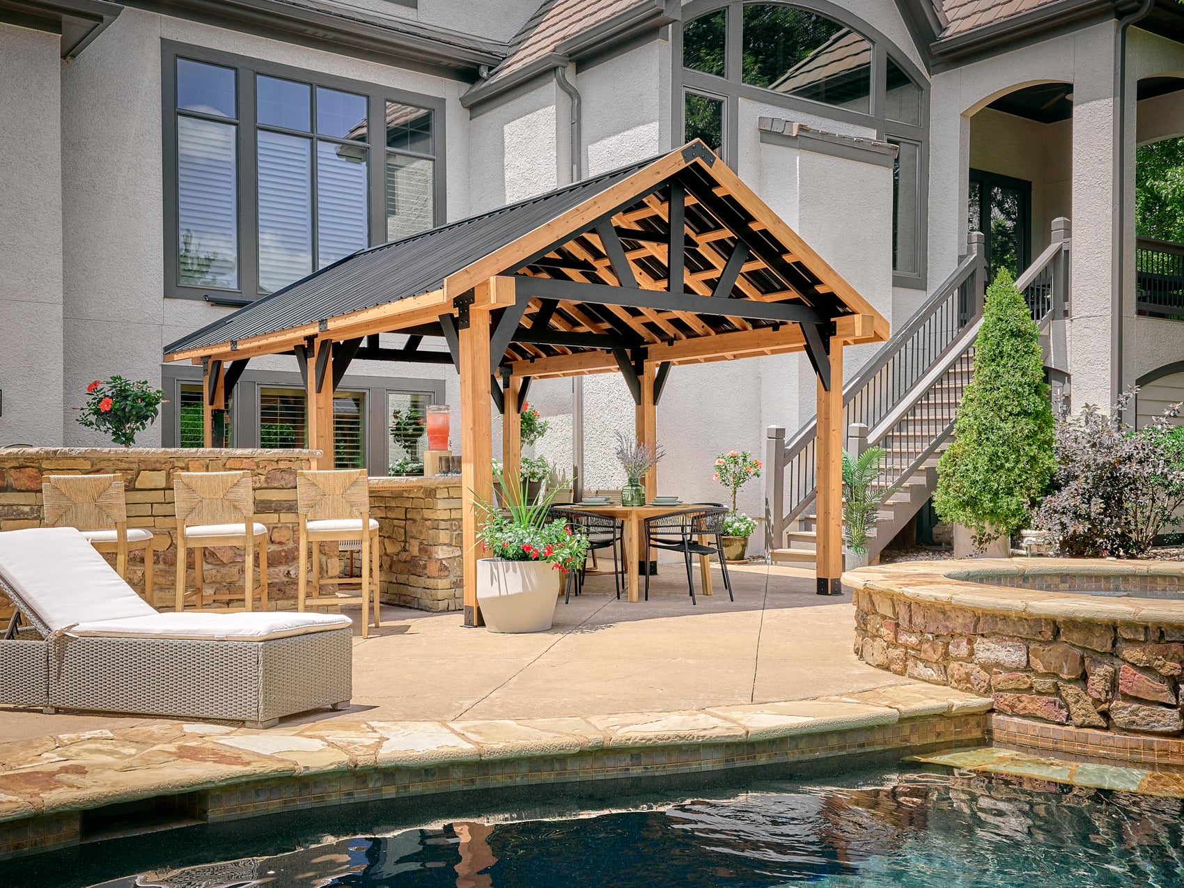 Modern Lodge gazebo with metal roof and timber-frame design beside pool with outdoor kitchen and patio furniture.