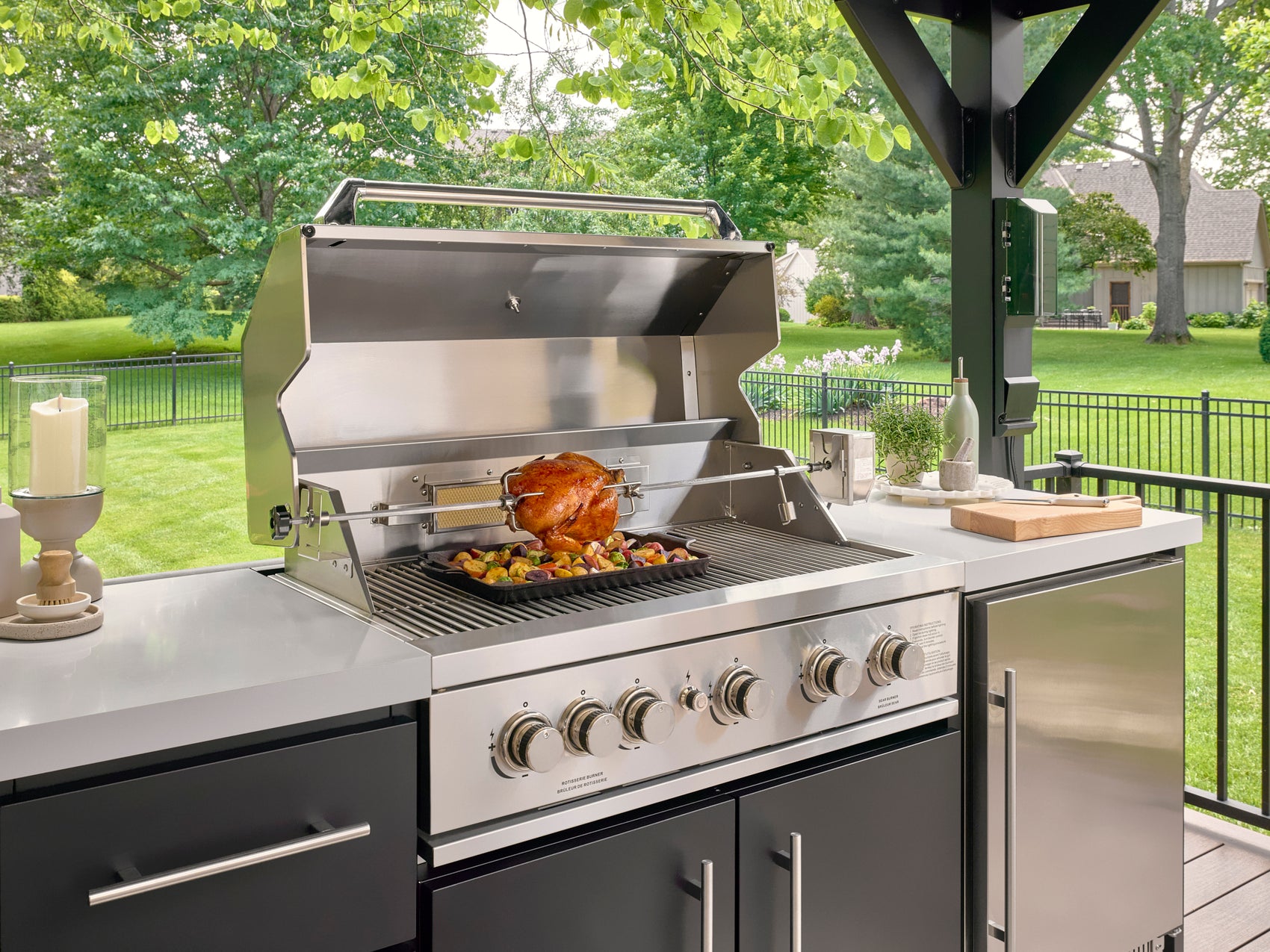 Rotisserie and side burner on built-in stainless steel grill under covered patio kitchen.
