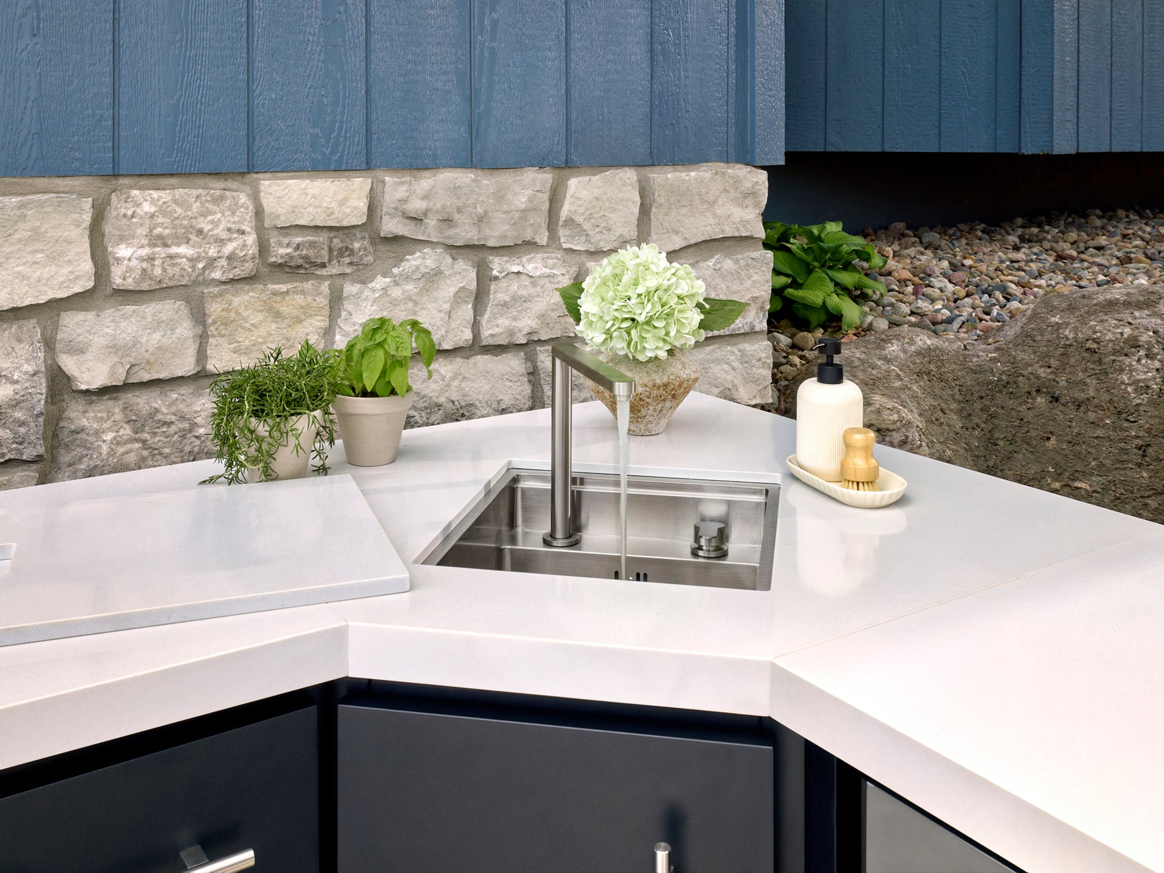 Emory Outdoor sink with modern faucet set in white engineered stone countertop with potted herbs and soap dispenser nearby.